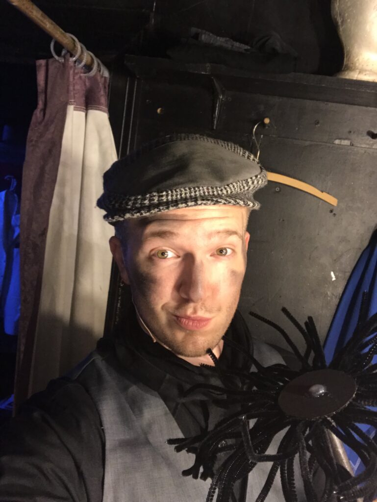  Darrell Wood takes a playful selfie backstage while wearing a cap and theatrical makeup, holding a large chimney sweeper prop.